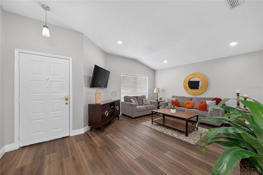 A living room features wood-look flooring, a gray sofa, a loveseat, and a front door — 8809 PARLIAMENT COURT, KISSIMMEE, FL