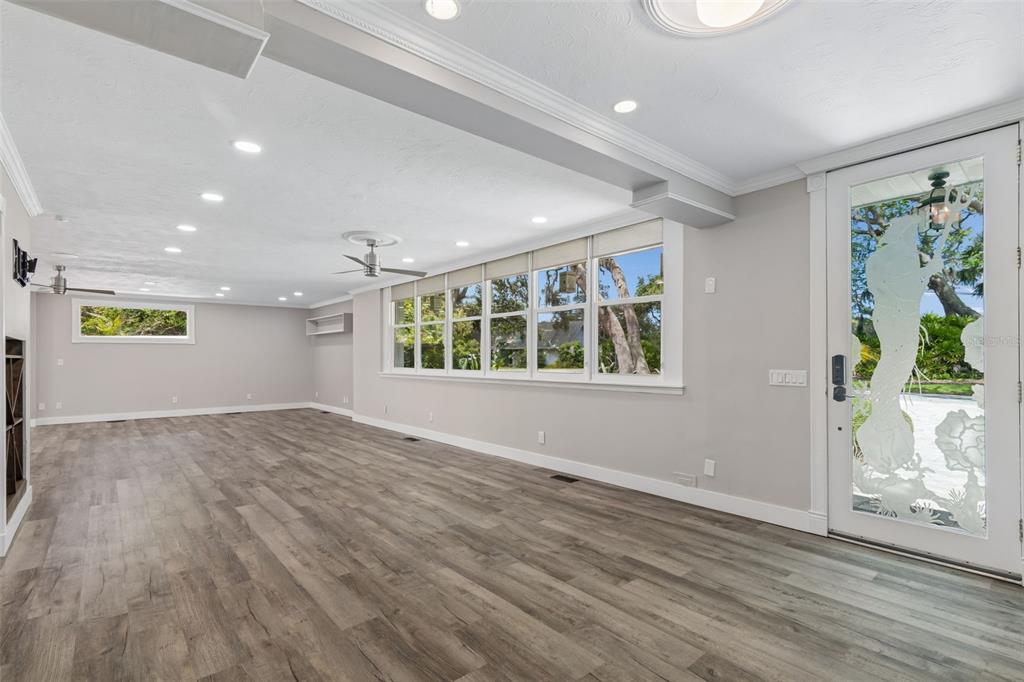 A spacious room with light wood-look flooring, recessed lighting, large windows, and a decorative glass door — 904 BAYSHORE DRIVE, TARPON SPRINGS, FL