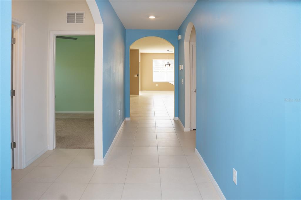 A hallway with blue walls and tile flooring leads to an arched entryway — 2614 GREENLEAF TERRACE, PARRISH, FL