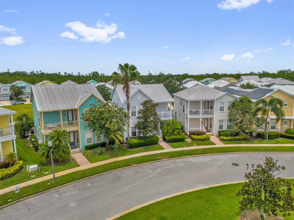 An aerial view shows three colorful, multi-story houses with metal roofs along a curved street — 7766 LINKSIDE LOOP, REUNION, FL