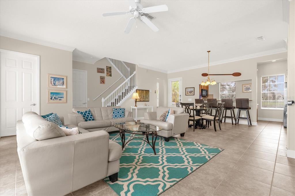 A living room with light tile floors, white sofas, a patterned rug, and a staircase — 7766 LINKSIDE LOOP, REUNION, FL