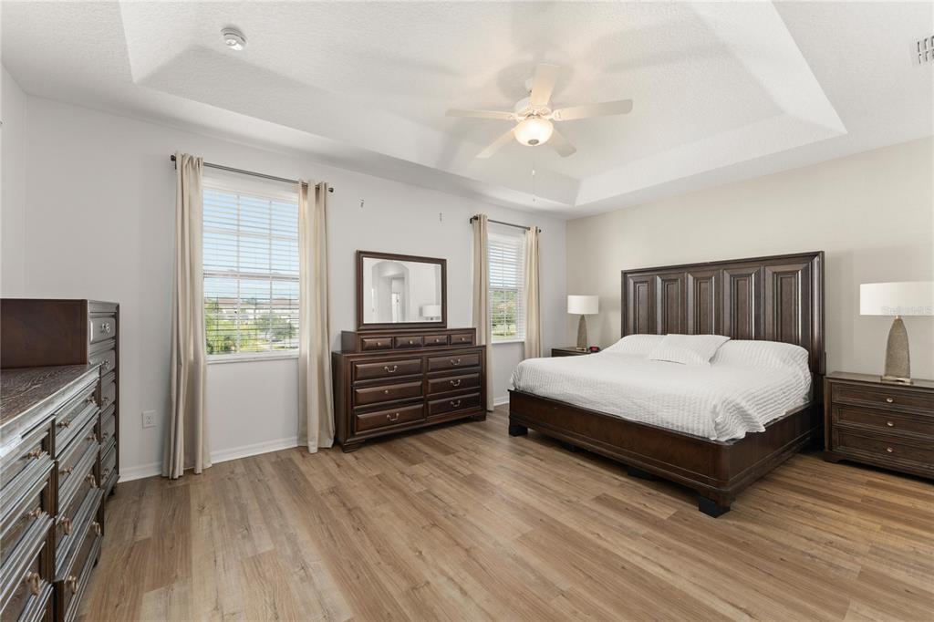 A bedroom features a tray ceiling, wood-look flooring, a large bed, and dark wood furniture — 4429 SHIVA LOOP, KISSIMMEE, FL