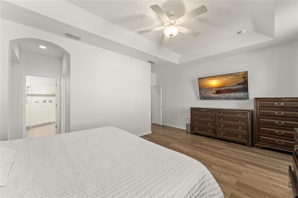A bedroom features a tray ceiling, ceiling fan, wood-look flooring, and a wall-mounted television — 4429 SHIVA LOOP, KISSIMMEE, FL