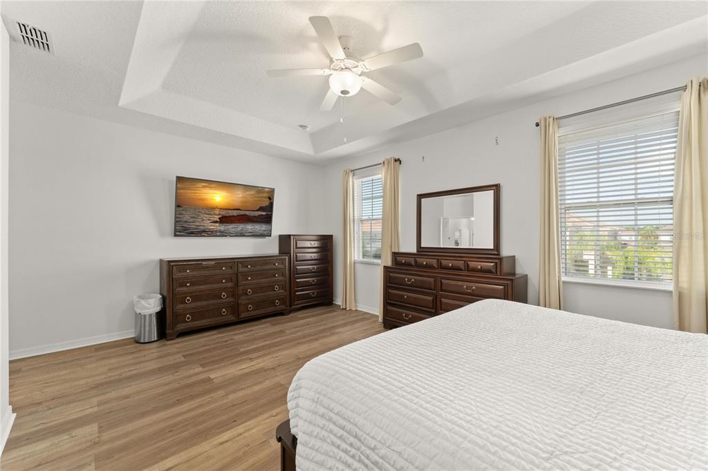 A bedroom features wood-look flooring, a tray ceiling with a fan, and dark wood furniture — 4429 SHIVA LOOP, KISSIMMEE, FL