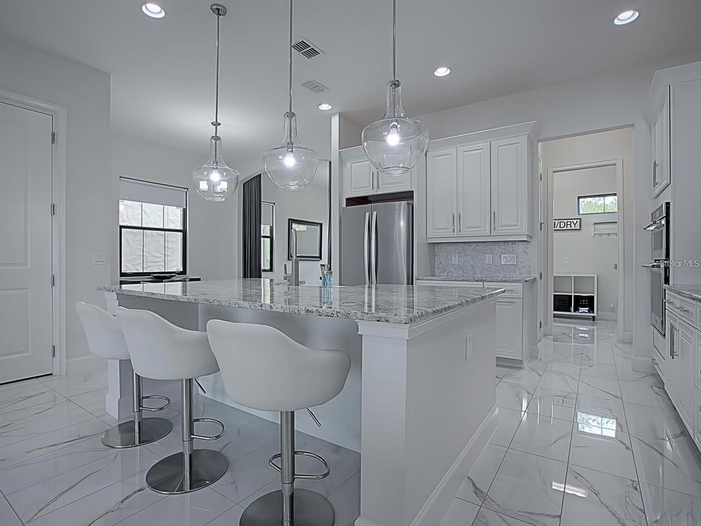 A modern white kitchen features a granite-topped island with three stools and marble-look tile flooring — 7661 TOSCANA BOULEVARD, ORLANDO, FL