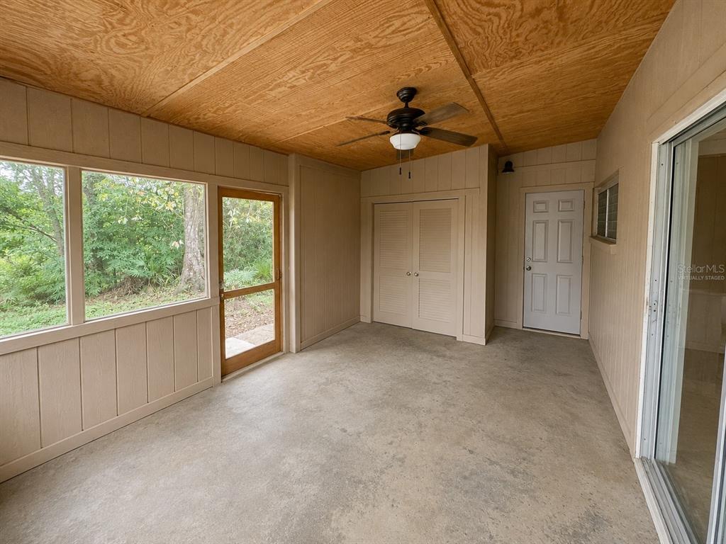 A screened-in porch with a wood-paneled ceiling, concrete floor, ceiling fan, and storage closet — 6013 IDLE A WHILE CIRCLE, DADE CITY, FL