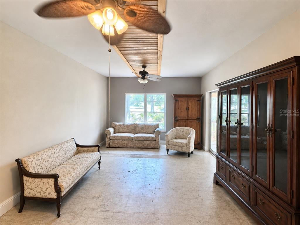 This living room features a wood-paneled ceiling accent, two ceiling fans, and tile flooring — 6013 IDLE A WHILE CIRCLE, DADE CITY, FL