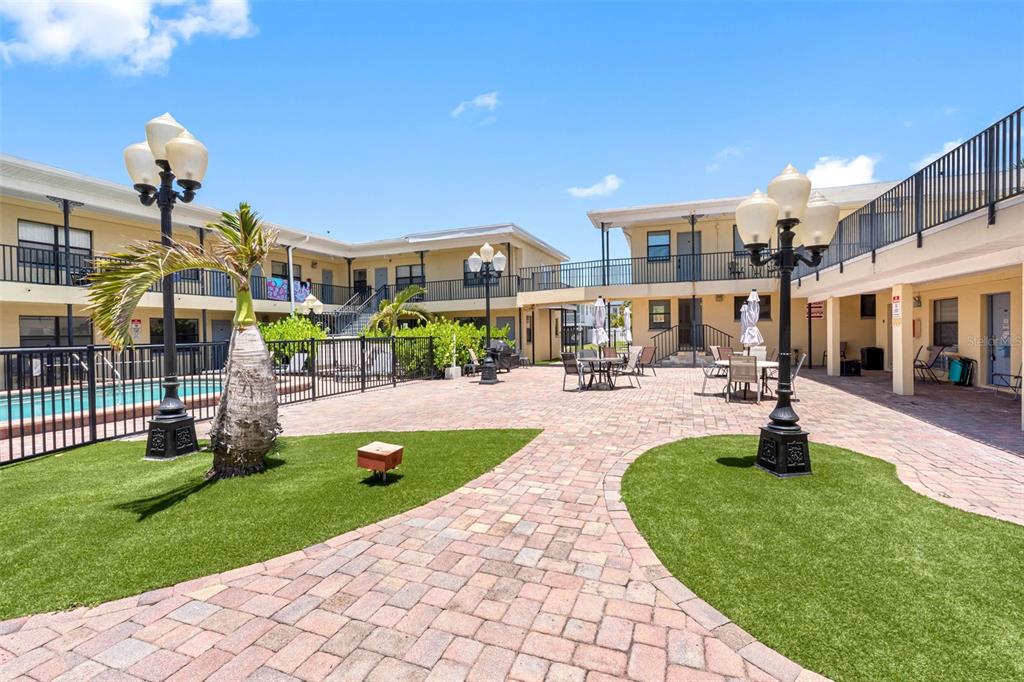 An outdoor courtyard with brick pavers, artificial turf, patio furniture, and two ornate lamp posts — 16333 GULF BOULEVARD UNIT 210, REDINGTON BEACH, FL
