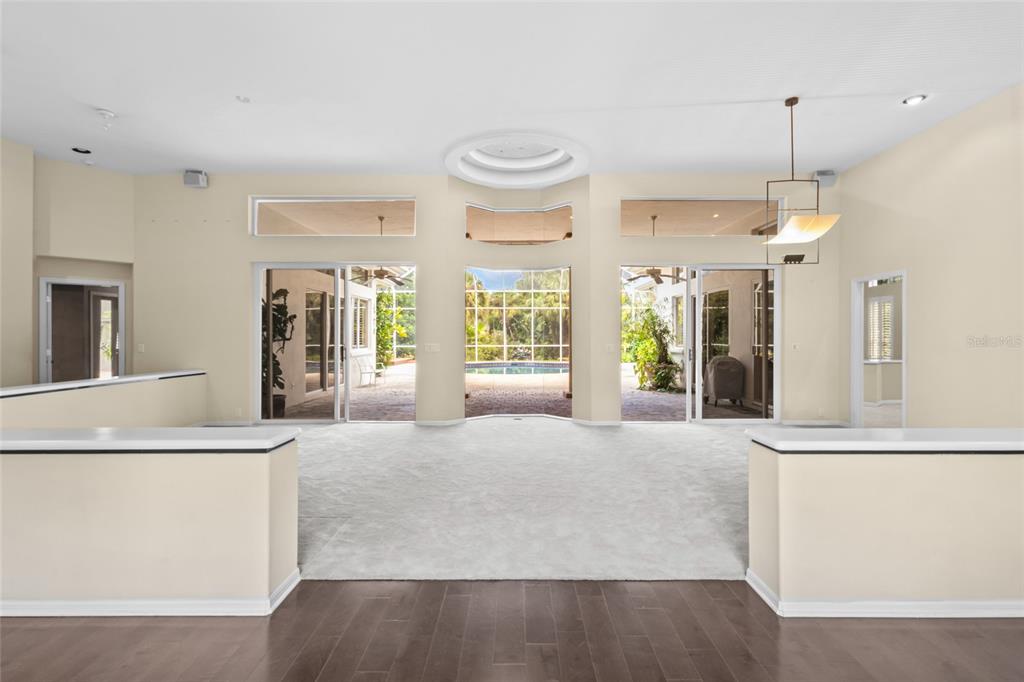 A spacious living room features light carpeting, hardwood flooring, and large sliding glass doors — 5166 KESTRAL PARK TERRACE, SARASOTA, FL