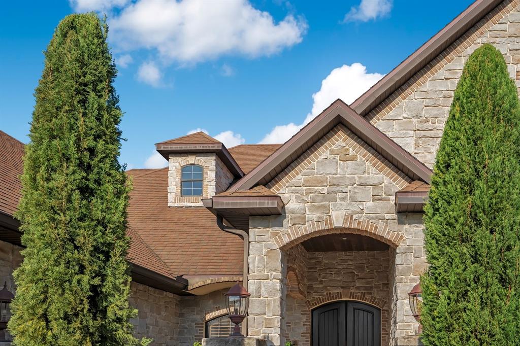 The exterior of a stone house features a gabled roof, a dormer window, and tall trees — 2310 NEVADA ROAD, LAKELAND, FL