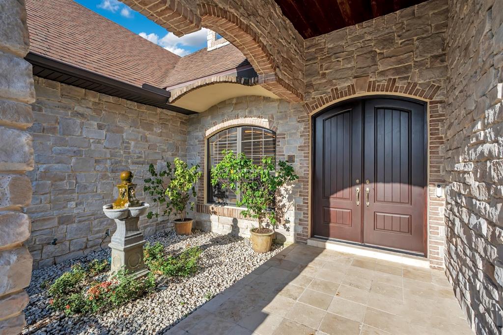 An arched stone entryway features a double front door, a small fountain, and potted plants — 2310 NEVADA ROAD, LAKELAND, FL