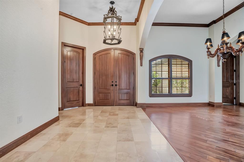 An entryway with tile flooring, wood double doors, and a chandelier transitions to a wood-floored room — 2310 NEVADA ROAD, LAKELAND, FL