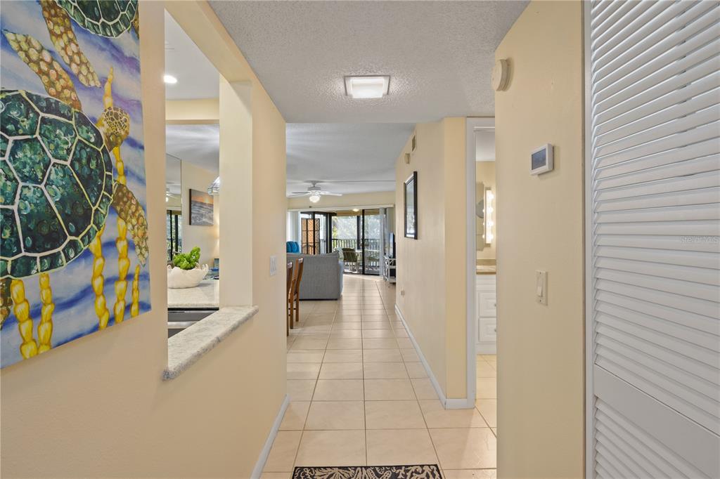 A hallway with tile flooring leads from an entryway into an open-concept living area — 5608 GULF DRIVE UNIT 104, HOLMES BEACH, FL