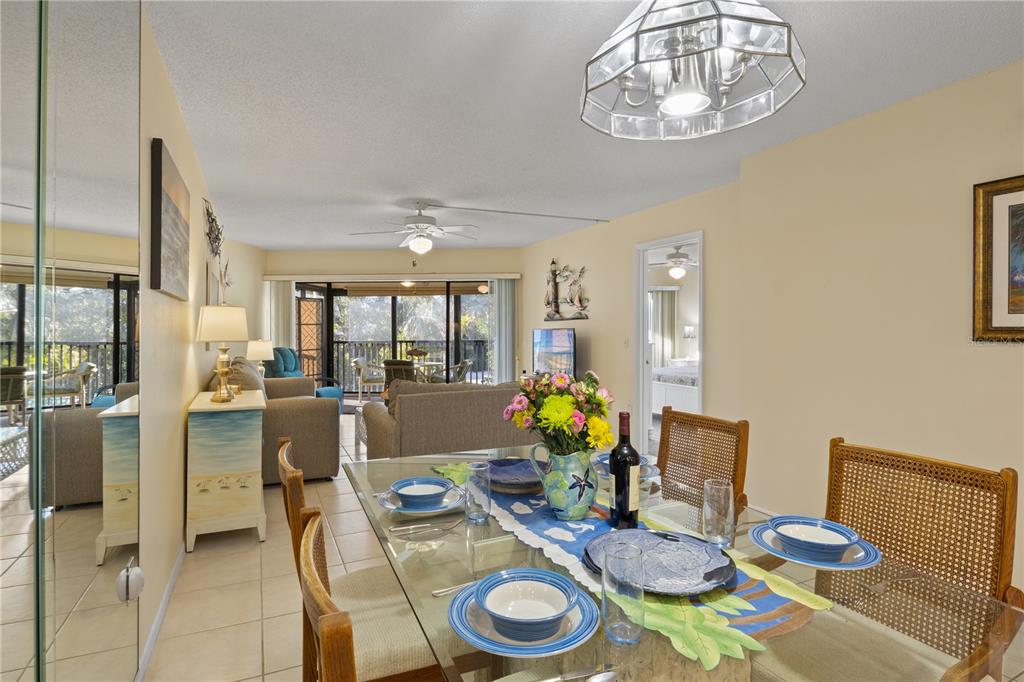 A dining area with a glass table leads into a living room with a balcony — 5608 GULF DRIVE UNIT 104, HOLMES BEACH, FL