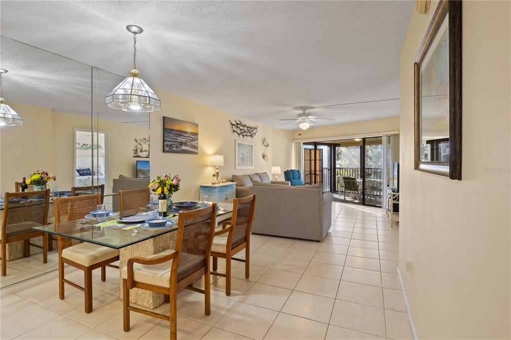 A dining area with a glass table and chairs opens into a living room with balcony — 5608 GULF DRIVE UNIT 104, HOLMES BEACH, FL