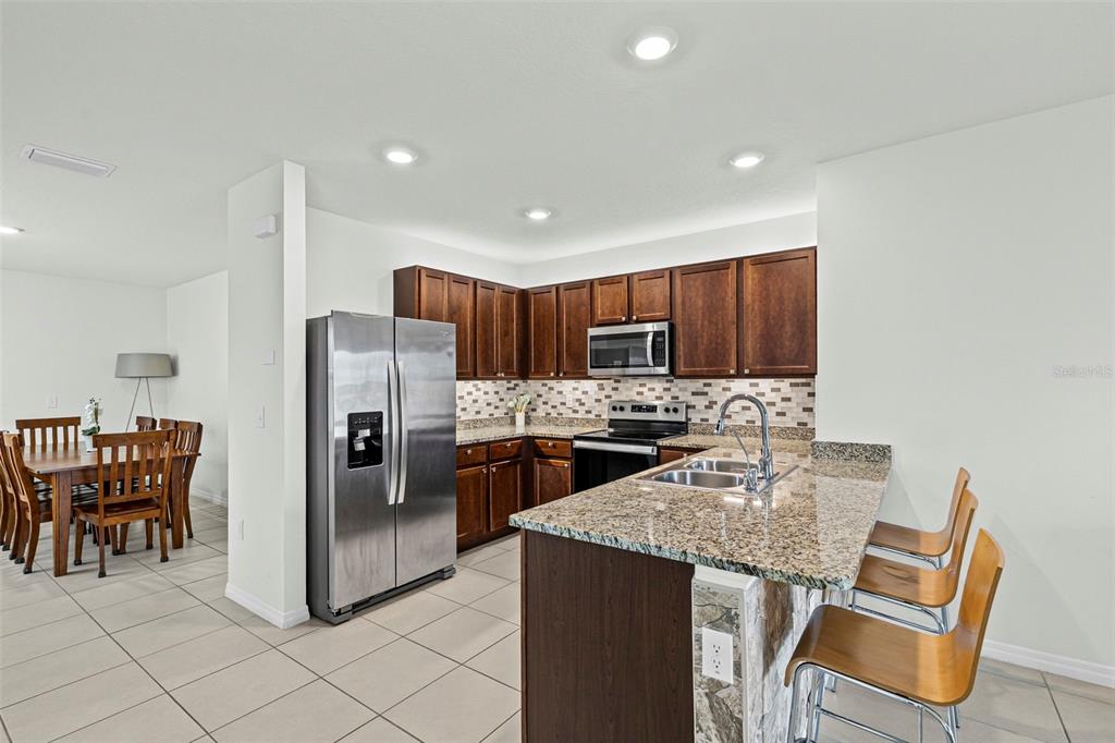 A kitchen with dark wood cabinets, granite countertops, stainless steel appliances, and a breakfast bar — 10914 PENNY GALE LOOP, SAN ANTONIO, FL