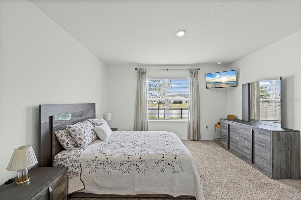 A bedroom with a bed, dresser, wall-mounted television, and a window overlooking a fenced yard — 10914 PENNY GALE LOOP, SAN ANTONIO, FL