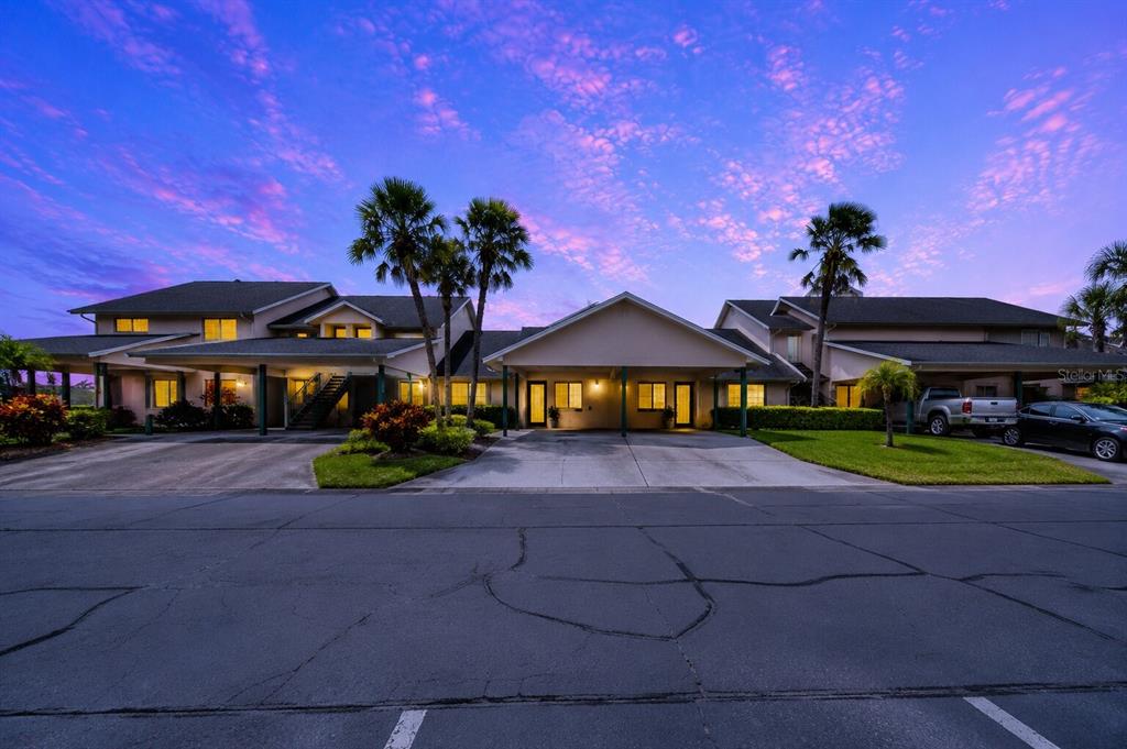 A two-story apartment building exterior features covered parking spaces and palm trees at dusk — 644 YARDARM DRIVE UNIT 22, APOLLO BEACH, FL