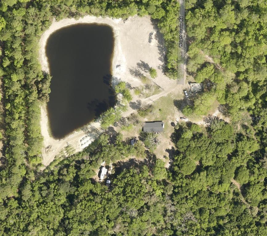 This aerial view shows a house and a pond surrounded by dense forest — 270 WRIGHT GROVE ROAD, OAK HILL, FL