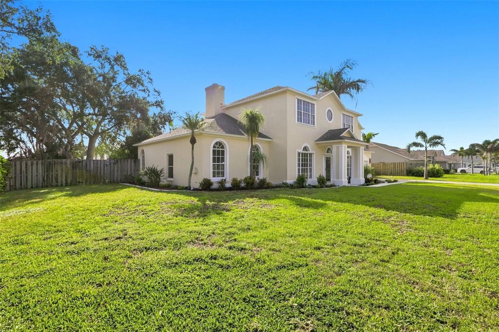 A two-story beige house with a chimney and arched windows sits on a grassy lot — 2520 MILLRACE WAY, MERRITT ISLAND, FL