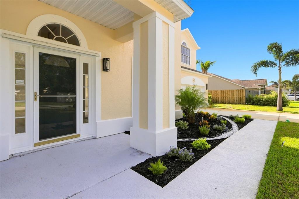A front porch with a white door, a large pillar, and a landscaped garden bed — 2520 MILLRACE WAY, MERRITT ISLAND, FL