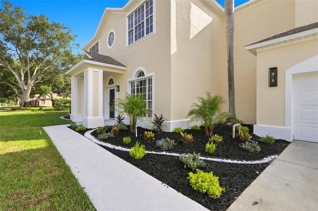 A beige two-story house exterior features a landscaped garden bed with mulch and white stones — 2520 MILLRACE WAY, MERRITT ISLAND, FL