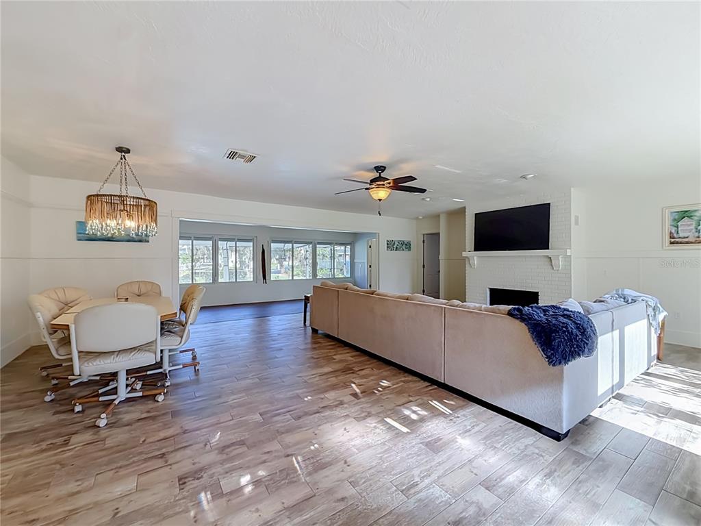 An open-concept living and dining area features wood-look tile flooring, a brick fireplace, and a chandelier — 536 NW 9TH AVENUE, CRYSTAL RIVER, FL