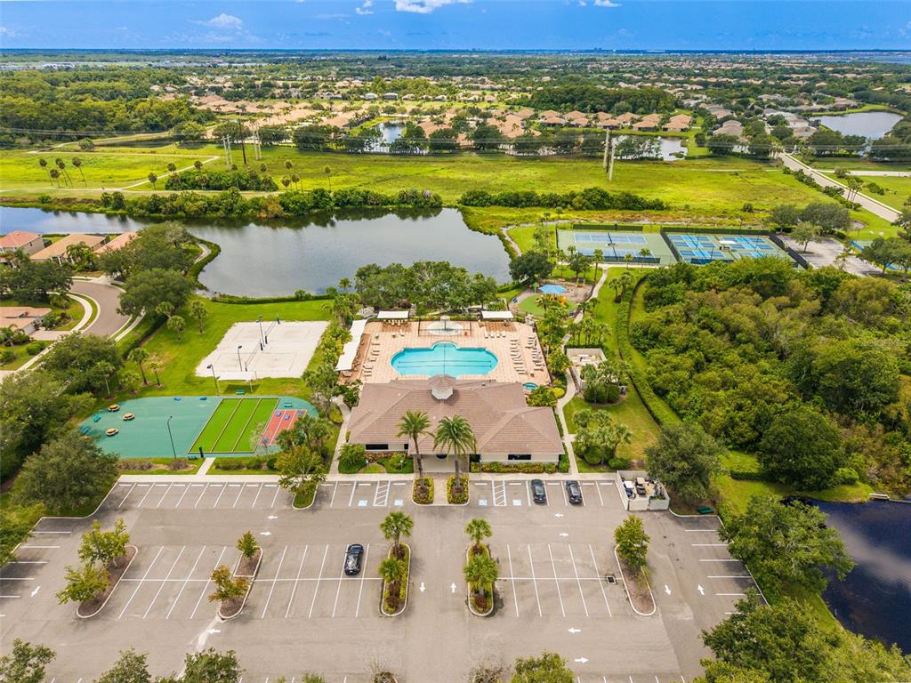 An aerial view shows a community clubhouse with a pool, sports courts, and parking lot — 8815 BROOKFIELD TERRACE, BRADENTON, FL