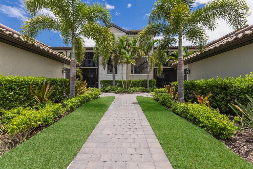 A paved walkway leads through a landscaped courtyard toward a two-story apartment building with palms — 5721 PALMER CIRCLE UNIT 103, BRADENTON, FL
