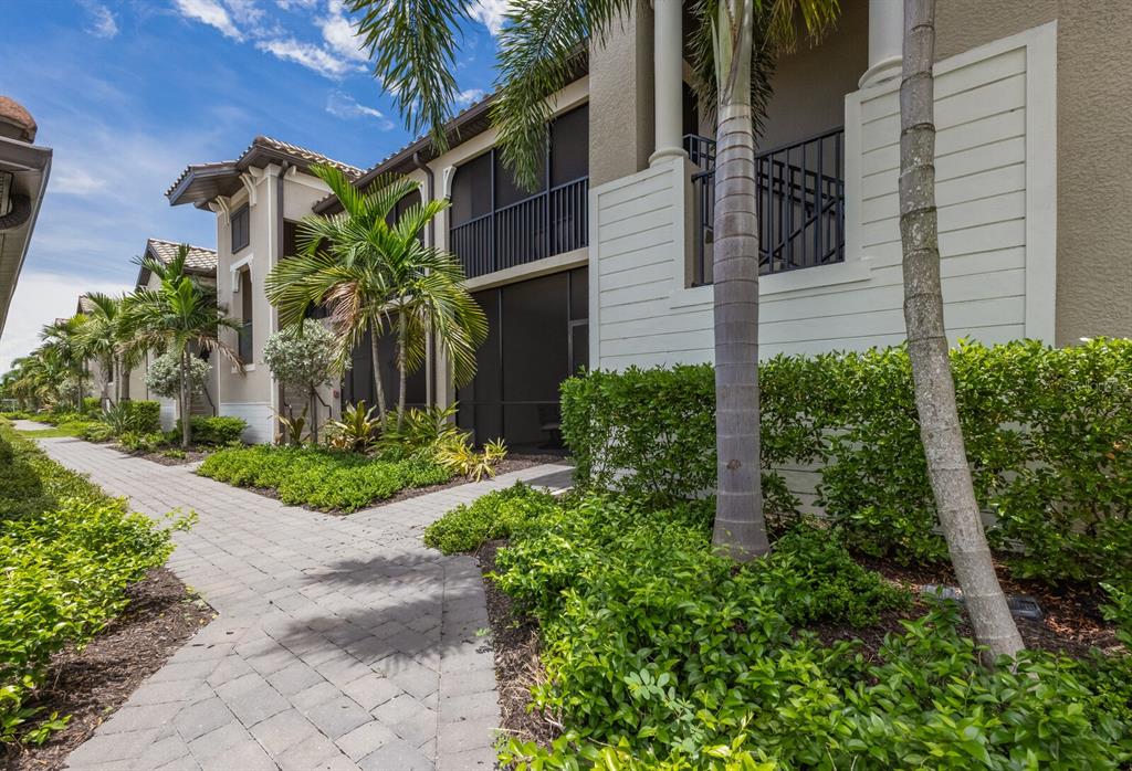 A paved walkway leads past palm trees and landscaped bushes toward a two-story apartment building — 5721 PALMER CIRCLE UNIT 103, BRADENTON, FL