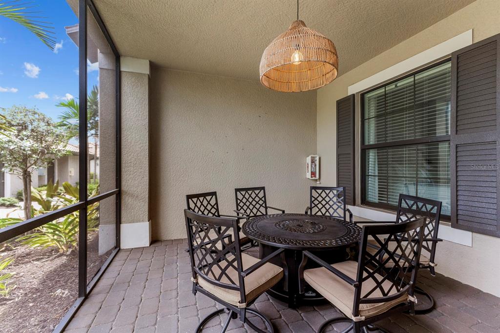 A screened-in patio features a round metal dining set, a woven pendant light, and pavers — 5721 PALMER CIRCLE UNIT 103, BRADENTON, FL