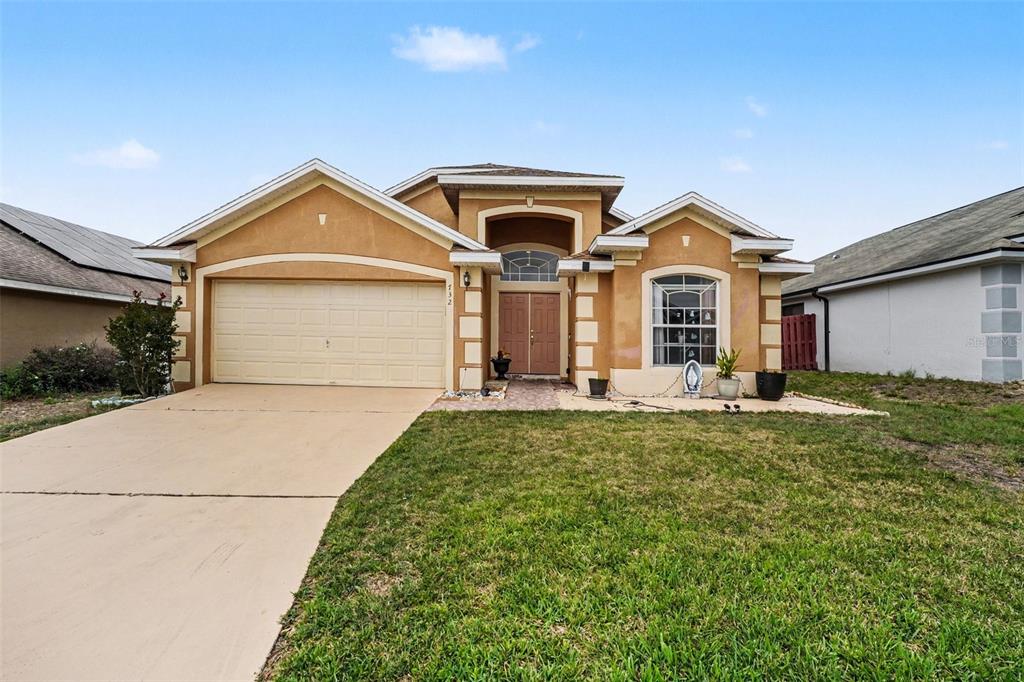 A single-story tan stucco house with a two-car garage and a front-facing arched window — 732 GLENCO DRIVE, DAVENPORT, FL