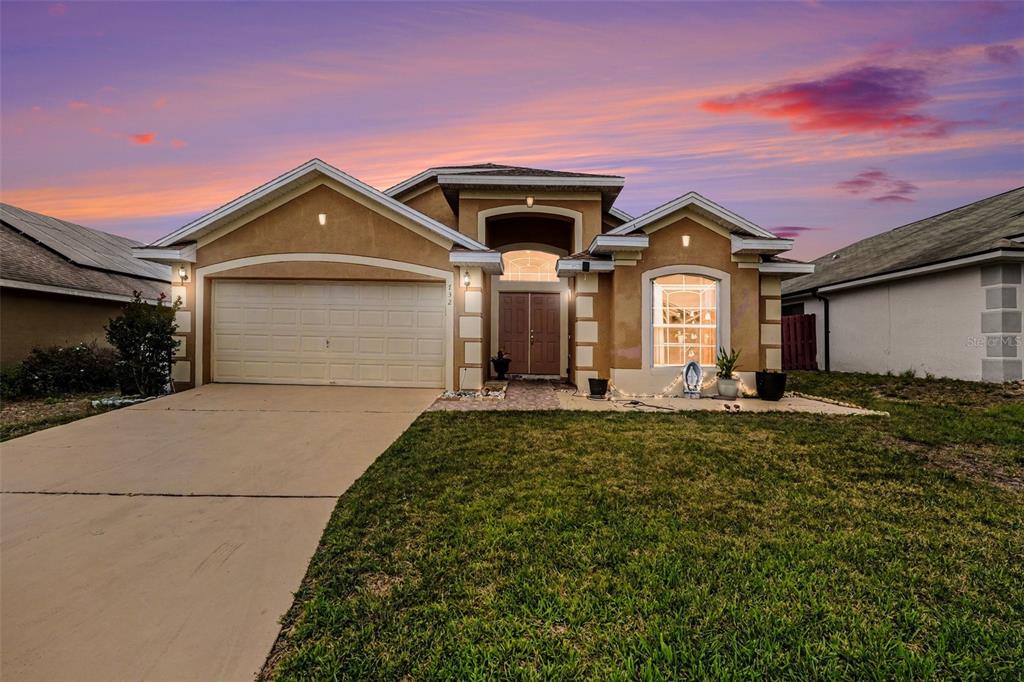 A single-story suburban house with a tan stucco exterior, a two-car garage, and a front lawn — 732 GLENCO DRIVE, DAVENPORT, FL