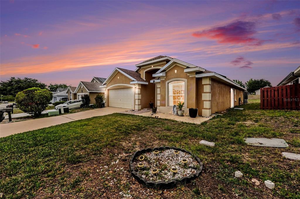 A single-story suburban house with a tan stucco exterior, two-car garage, and a sunset sky — 732 GLENCO DRIVE, DAVENPORT, FL