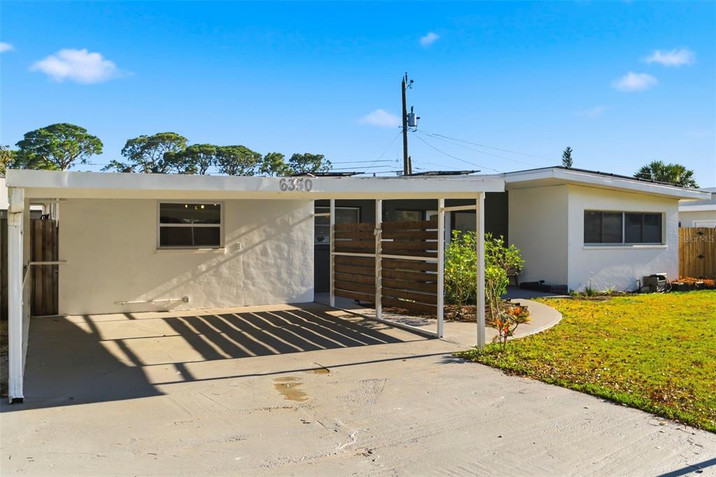 A single-story house with a white exterior, a carport, and a wooden privacy screen — 6350 HAMPTON DRIVE N, ST PETERSBURG, FL