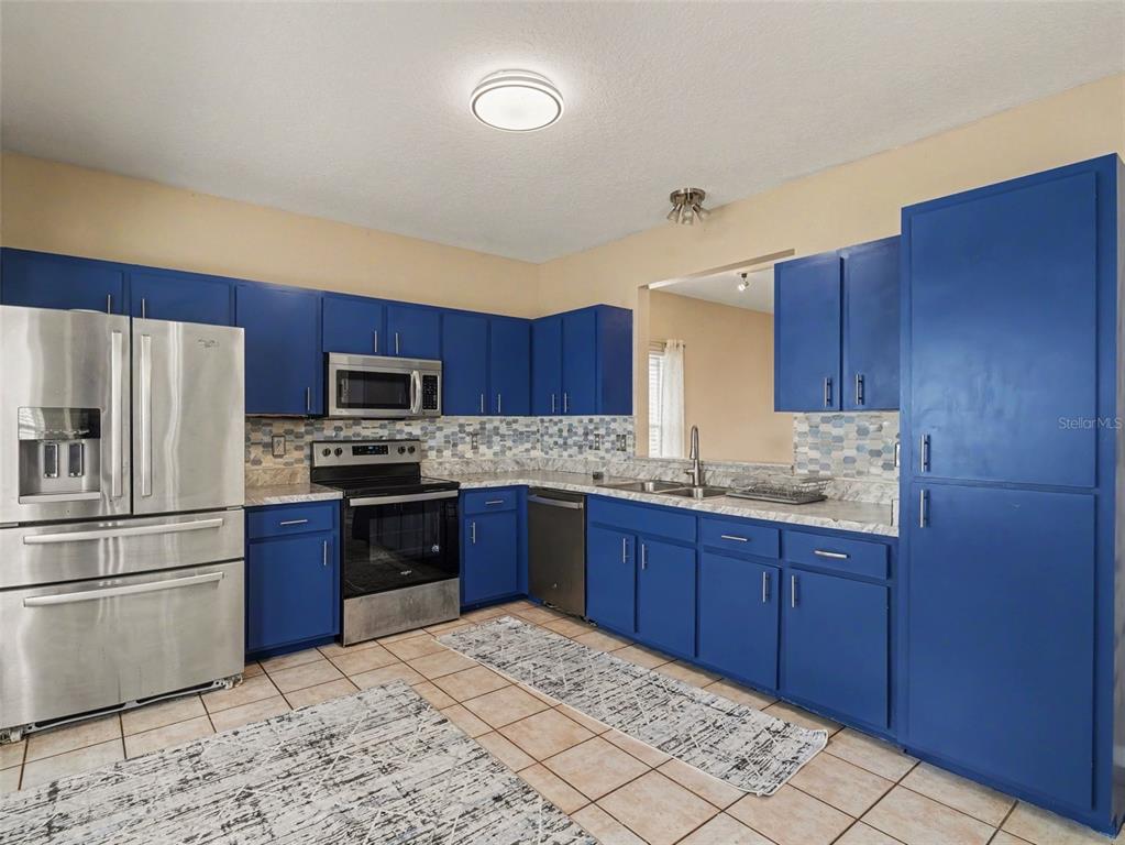 A kitchen features blue cabinets, stainless steel appliances, a tiled backsplash, and light-colored tile flooring — 3715 E 31ST STREET, BRADENTON, FL