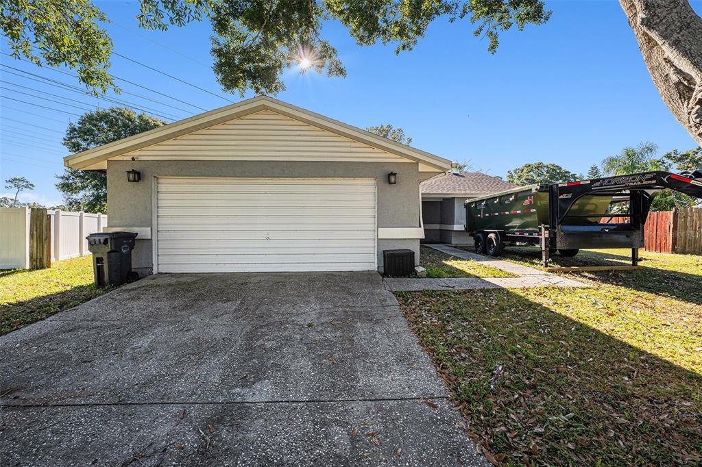 A single-story house with a white garage door, a concrete driveway, and a large dump trailer — 645 TIMBER BAY CIRCLE E, OLDSMAR, FL