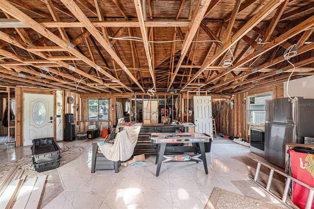 An unfinished room with exposed wooden ceiling trusses, tiled flooring, and a central air hockey table — 645 TIMBER BAY CIRCLE E, OLDSMAR, FL