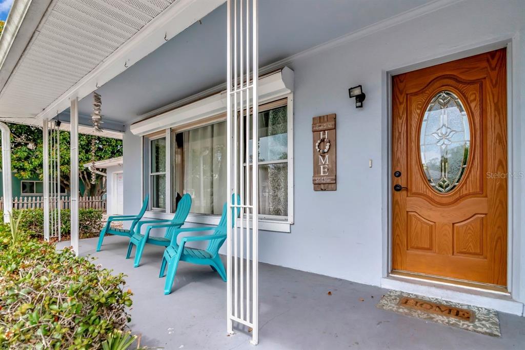 A covered front porch features light blue walls, two turquoise chairs, and a wooden front door — 305 BAKER AVENUE, CLEARWATER, FL