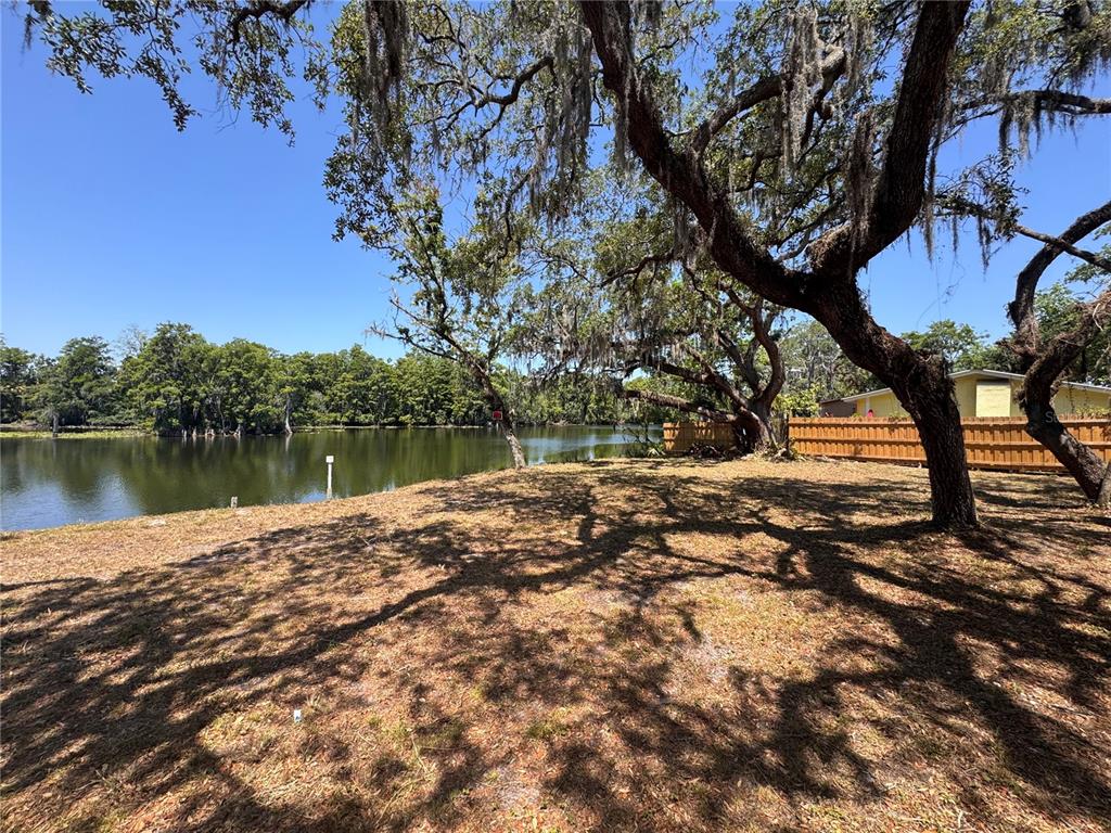 A grassy yard with large oak trees overlooks a calm lake next to a wooden fence — HARNEY, TAMPA, FL