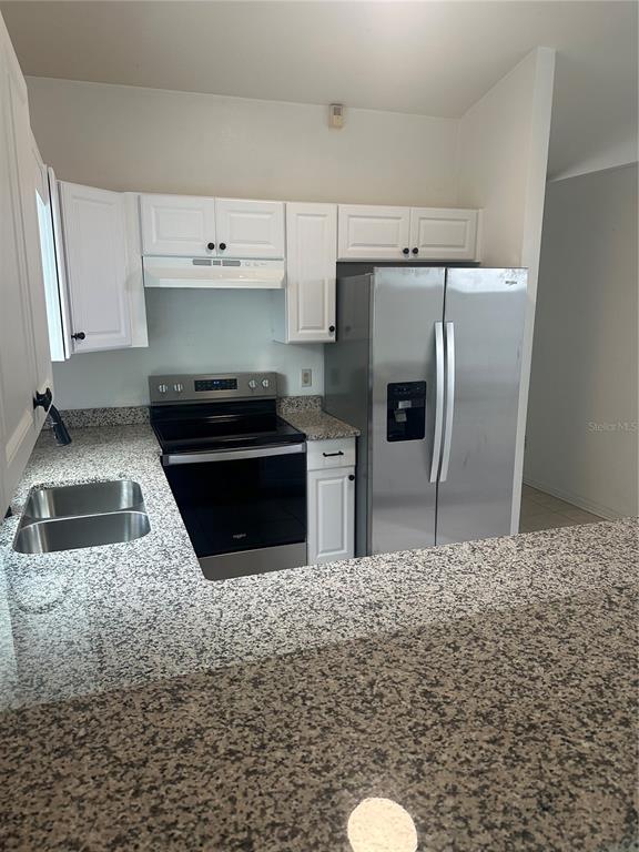 A kitchen features white cabinets, granite countertops, a stainless steel refrigerator, and a black stove — 3909 SW 161ST LOOP, OCALA, FL