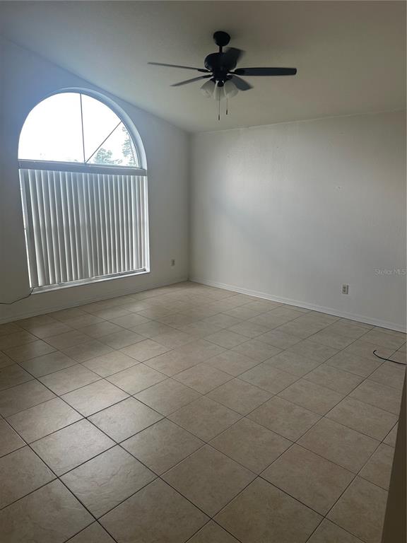 An empty room with tiled floors, a ceiling fan, and a large arched window — 3909 SW 161ST LOOP, OCALA, FL