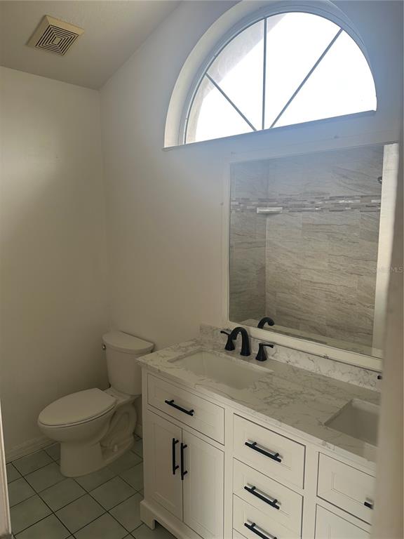 A bathroom features a white vanity with a marble countertop, a toilet, and an arched window — 3909 SW 161ST LOOP, OCALA, FL