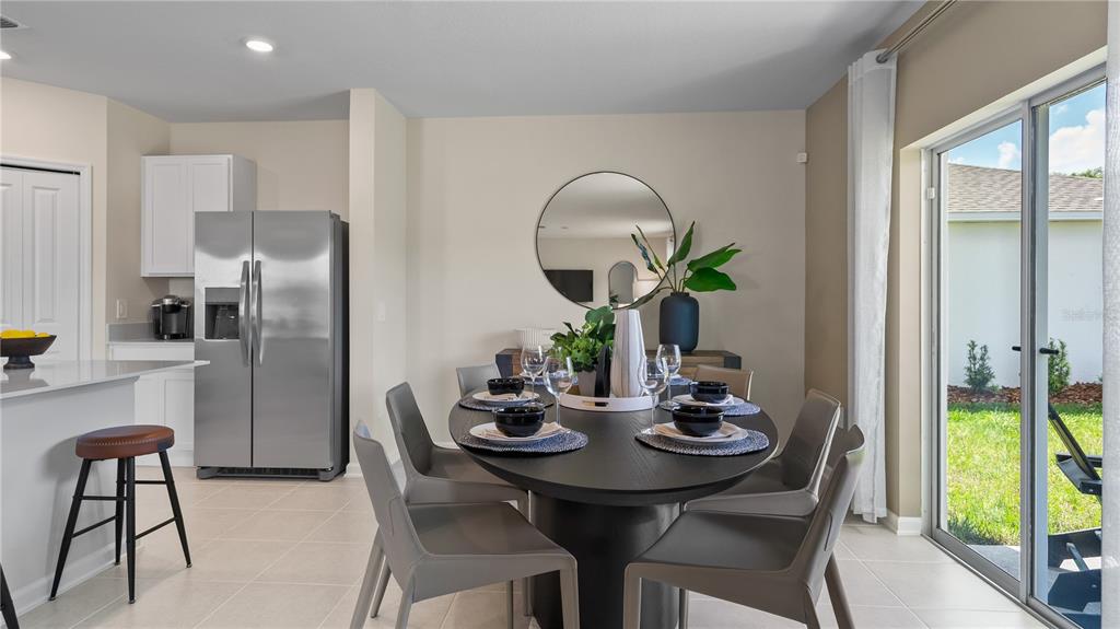 A dining area with a dark oval table, grey chairs, and a stainless steel refrigerator — 2473 HALLOW GARDEN ROAD, EUSTIS, FL