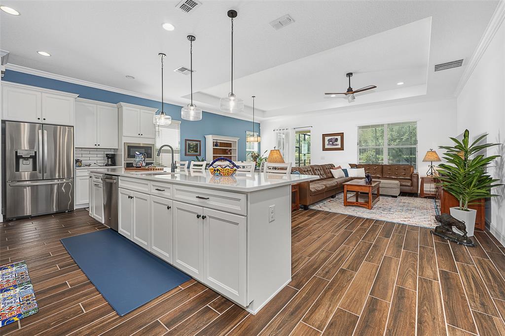 A kitchen with a white island and cabinets opens into a living room with wood floors — 7748 FOUR SEASONS BOULEVARD, KISSIMMEE, FL
