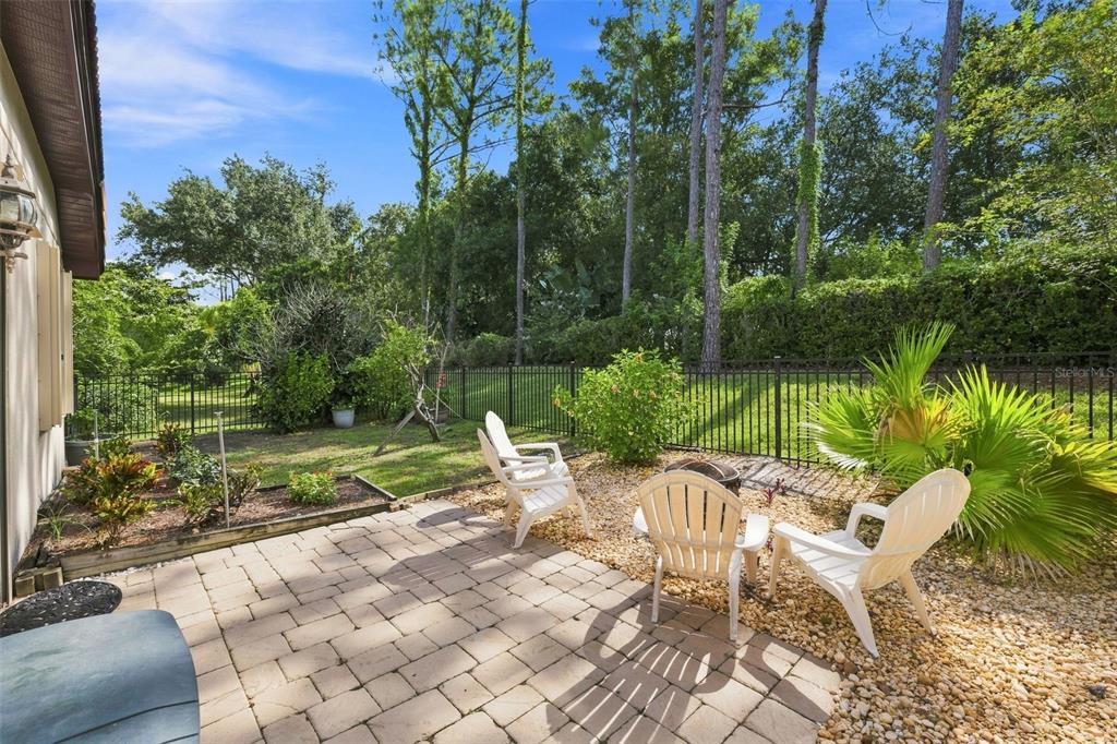 A paved patio with white chairs sits in a backyard enclosed by a black metal fence — 5091 JASMINE WAY, PALM HARBOR, FL