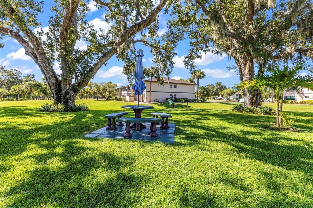 A picnic table with a closed blue umbrella sits on a patio in a grassy yard — 19505 QUESADA AVENUE UNIT T203, PORT CHARLOTTE, FL