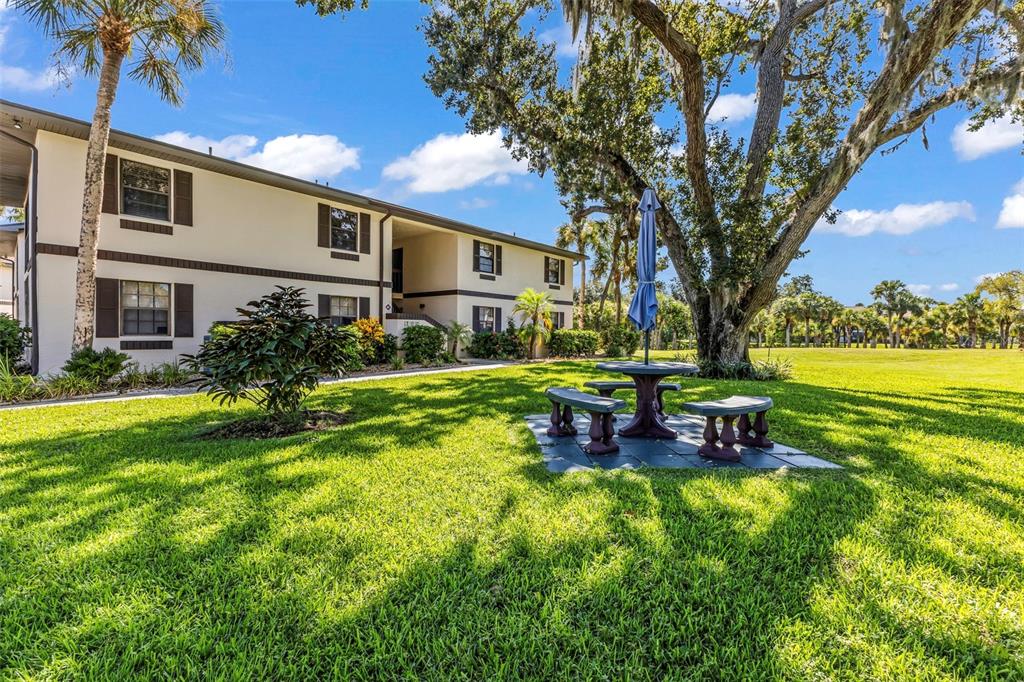 An outdoor picnic table with an umbrella sits on a lawn beside an apartment building — 19505 QUESADA AVENUE UNIT T203, PORT CHARLOTTE, FL