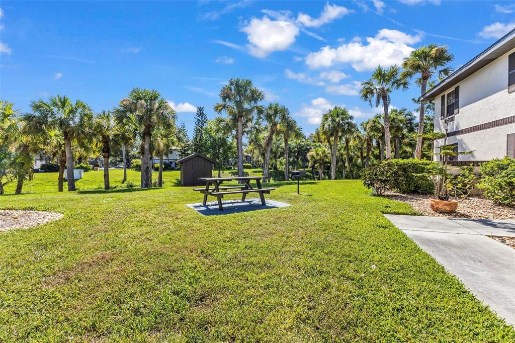 A grassy courtyard features a picnic table, palm trees, and a small shed near a building — 19505 QUESADA AVENUE UNIT T203, PORT CHARLOTTE, FL