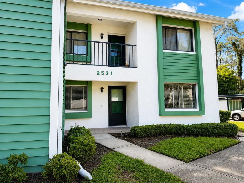 A two-story building exterior features white stucco walls, green trim, and a second-floor balcony — 2531 ROYAL PINES CIRCLE UNIT 23E, CLEARWATER, FL